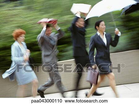 Stock Image - Group of business people running in rain, blurred. Fotosearch