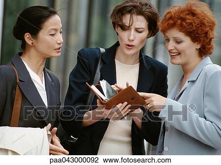 Stock Image - Three businesswomen side by side, one holding agenda. Fotosearch