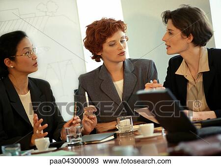 Three businesswomen sitting at conference table, talking View Large Photo Image Stock Image - Three businesswomen sitting at conference table, talking. Fotosearch