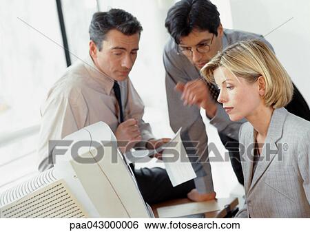 Stock Photograph - Two businessmen examining document, businesswoman looking at computer. Fotosearch