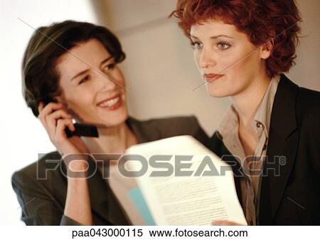 Two businesswomen side by side, one using phone View Large Photo Image Stock Photography - Two businesswomen side by side, one using phone. Fotosearch