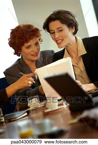 Two businesswomen sitting, looking at document View Large Photo Image Stock Photo - Two businesswomen sitting, looking at document. Fotosearch