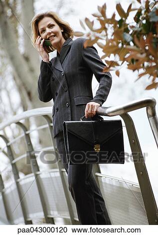 Stock Image - Woman leaning on rail outside, using cell phone, low angle view. Fotosearch