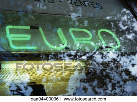 Stock Image - Euro text, neon sign, and tree reflection on glass, close-up. Fotosearch