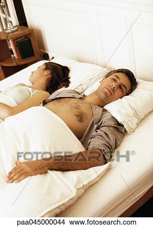 Picture - Couple lying in bed with heads turned in opposite directions. Fotosearch