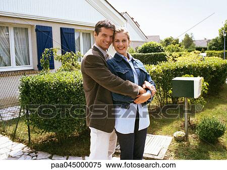 Couple standing in front of house, embracing View Large Photo Image Stock Photography - Couple standing in front of house, embracing. Fotosearch