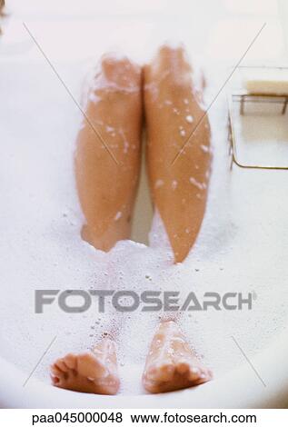 Stock Photo - Legs in bathtub surrounded by foam, close-up. Fotosearch