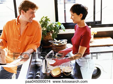 Picture - Man and woman in kitchen, looking at each other over counter, woman washing dishes. Fotosearch