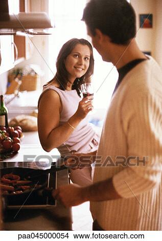 Picture - Man cooking, woman holding glass, blurred foreground. Fotosearch