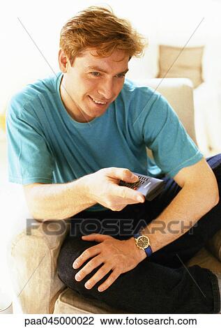 Stock Image - Man sitting, holding remote control, close-up. Fotosearch