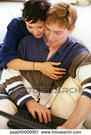 Stock Image - Man using laptop computer, woman with arm around him, waist up. Fotosearch