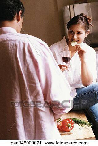 Stock Image - Woman eating and holding glass, rear view of man in foreground, blurred. Fotosearch