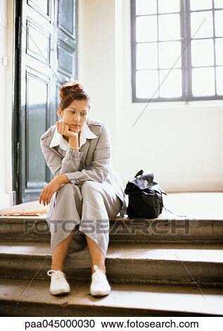 Stock Image - Woman sitting on steps, hand under chin, full length. Fotosearch