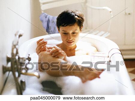 Stock Photo - Woman taking bath, holding leg out of water. Fotosearch