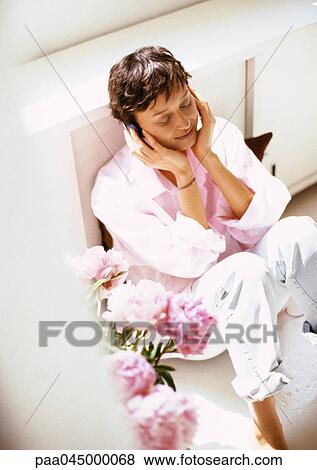 Stock Photo - Woman with hands to ears, smiling, sitting with knees up, high angle view. Fotosearch