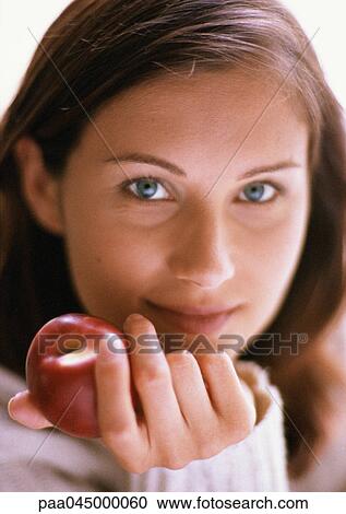Stock Image - Woman's head, hand holding red apple, close-up. Fotosearch