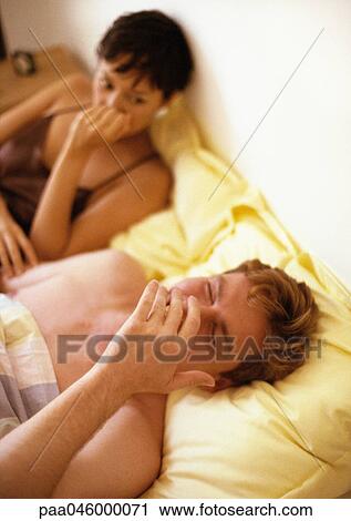 Couple lying in bed, man laughing, woman looking at him seriously View Large Photo Image Stock Image - Couple lying in bed, man laughing, woman looking at him seriously. Fotosearch