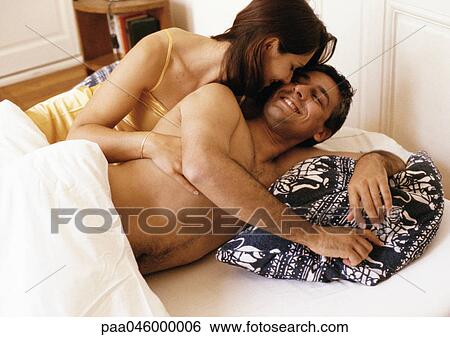 Stock Photograph - Couple lying in bed, woman hugging man from behind. Fotosearch