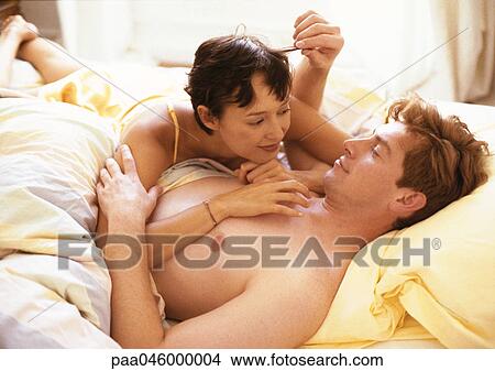 Couple lying in bed, woman lying on man's chest, man touching woman's hair View Large Photo Image Picture - Couple lying in bed, woman lying on man's chest, man touching woman's hair. Fotosearch
