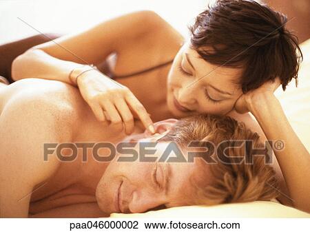 Couple lying in bed, woman touching man's ear View Large Photo Image Stock Image - Couple lying in bed, woman touching man's ear. Fotosearch