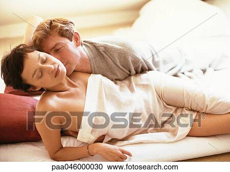 Couple lying in bed, woman wrapped in sheet, man behind her in t-shirt View Large Photo Image Stock Image - Couple lying in bed, woman wrapped in sheet, man behind her in t-shirt. Fotosearch