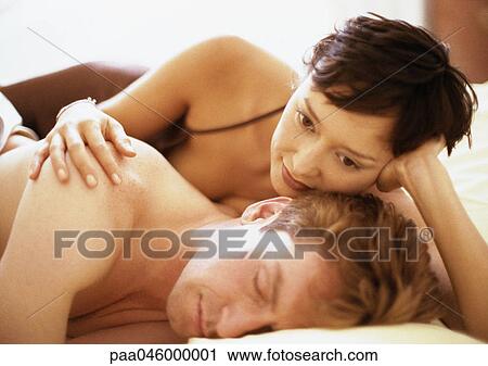 Couple lying in bed, woman's hand on man's shoulder View Large Photo Image Stock Image - Couple lying in bed, woman's hand on man's shoulder. Fotosearch