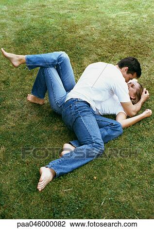 Stock Image - Couple lying on grass, man leaning over woman. Fotosearch