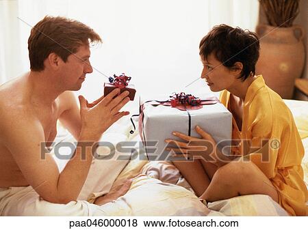 Couple sitting on bed face to face, exchanging presents View Large Photo Image Stock Photo - Couple sitting on bed face to face, exchanging presents. Fotosearch