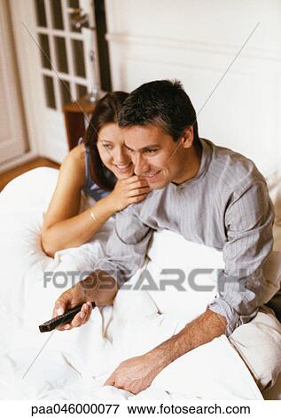 Couple sitting on bed, man holding remote control View Large Photo Image Stock Photo - Couple sitting on bed, man holding remote control. Fotosearch
