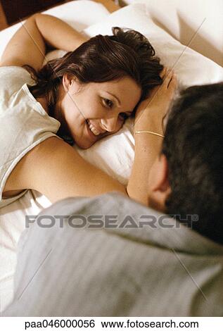 Woman lying on bed, looking at man in foreground View Large Photo Image Stock Photograph - Woman lying on bed, looking at man in foreground. Fotosearch
