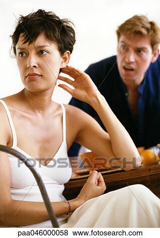 Stock Photo - Woman sitting at table, head turned away, man in background leaning across table toward her. Fotosearch