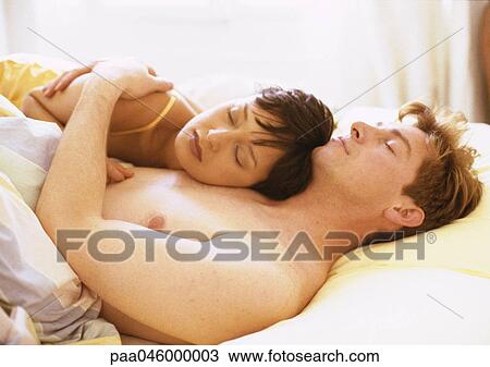 Stock Image - Woman with head on man's chest in bed, eyes closed. Fotosearch