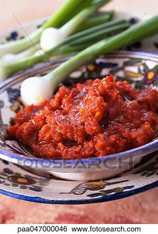 Stock Photograph - Harissa in bowl with spring onions in background, close-up. Fotosearch