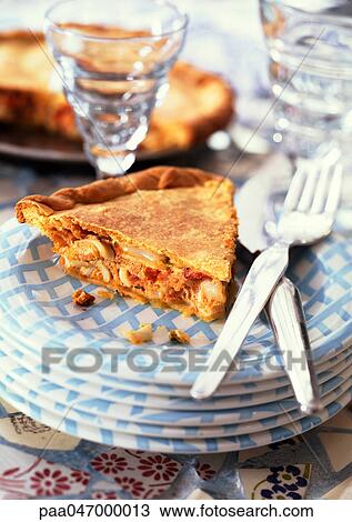Stock Image - Slice of seafood pie on stack of plates with knife and fork, close-up. Fotosearch