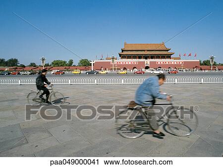 Stock Image - China, Beijing, two people riding bicycles in street in front of The Forbidden City. Fotosearch