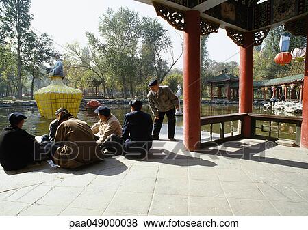 Stock Photo - China, Xinjiang Province, Urumqi, group of men sitting on ground, park in background. Fotosearch