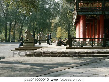 Stock Image - China, Xinjiang Province, Urumqi, people sitting in front of temple. Fotosearch