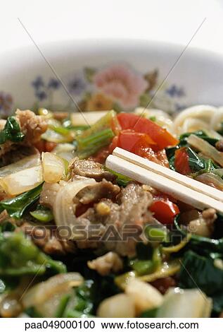 Stock Image - Chopsticks in dish of meat and vegetables, close-up. Fotosearch