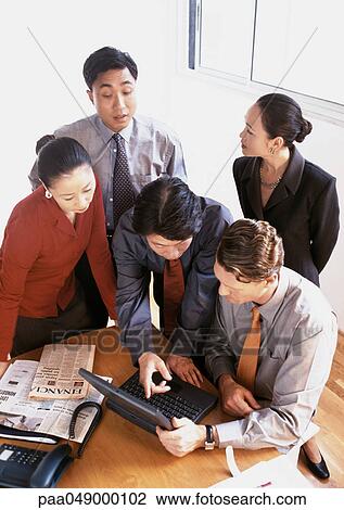Stock Image - Five people gathered around laptop computer on desk, high angle view. Fotosearch