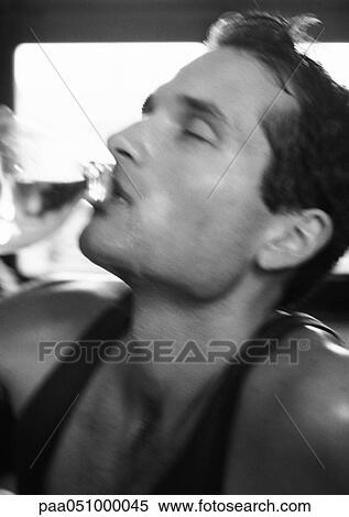Stock Photography - Man drinking from bottle with eyes closed, close-up, blurred, b&w. Fotosearch