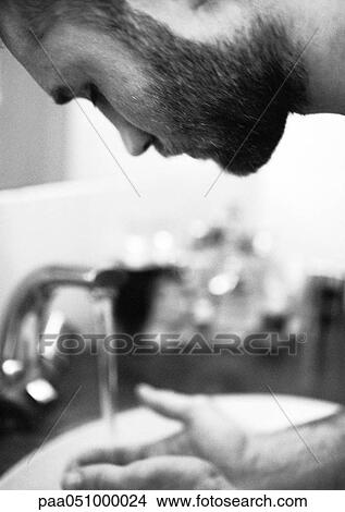 Picture - Man leaning forward, hands under tap, b&w. Fotosearch