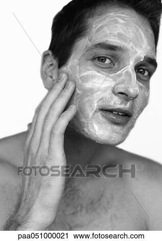 Stock Image - Man putting cream on face, portrait, b&w. Fotosearch