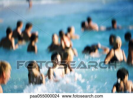 Picture - People standing waist-deep in water at beach, blurred. Fotosearch