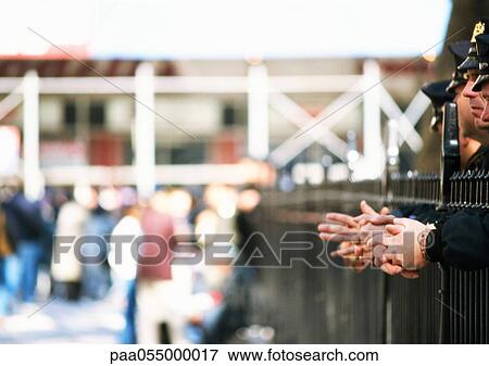 Stock Photo - Police standing behind railings, partial side view, crowd in background, blurred. Fotosearch