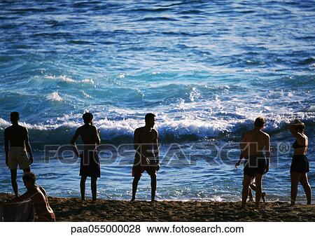 Silhouettes of people standing on beach at edge of sea, waves in background View Large Photo Image Stock Photo - Silhouettes of people standing on beach at edge of sea, waves in background. Fotosearch