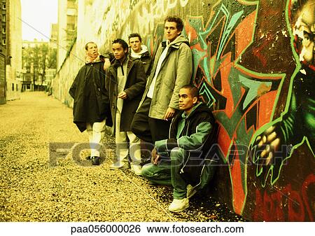 Stock Photograph - Five young men leaning against wall covered in graffiti, full length. Fotosearch