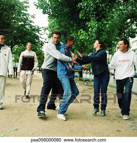 Stock Image - Group of young people in park, two play fighting. Fotosearch