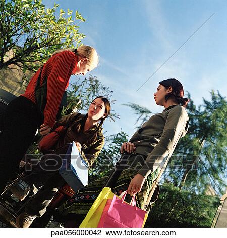 Stock Image - Three teenage girls holding shopping bags, low angle view. Fotosearch