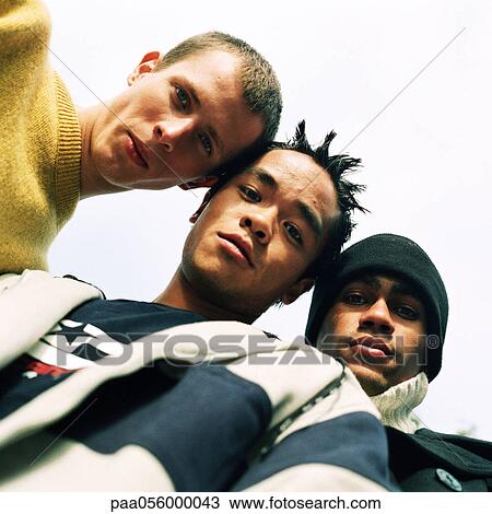 Stock Image - Three young men looking into camera, low angle view. Fotosearch