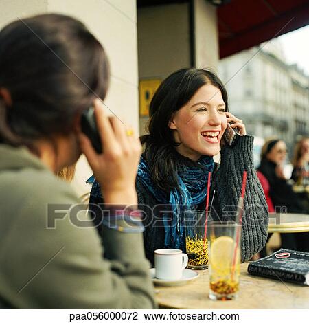 Stock Image - Two teenage girls sitting at cafe terrace, holding cell phones. Fotosearch